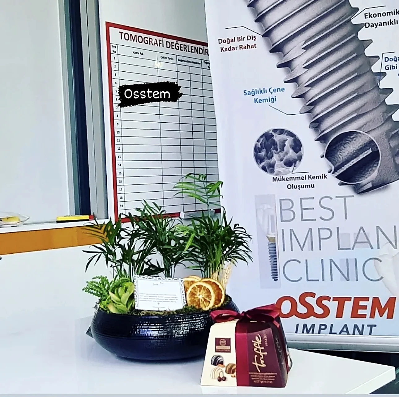 Klinik içi bir masada bir Osstem Implant banner'ı ve bir tomografi değerlendirme panosu