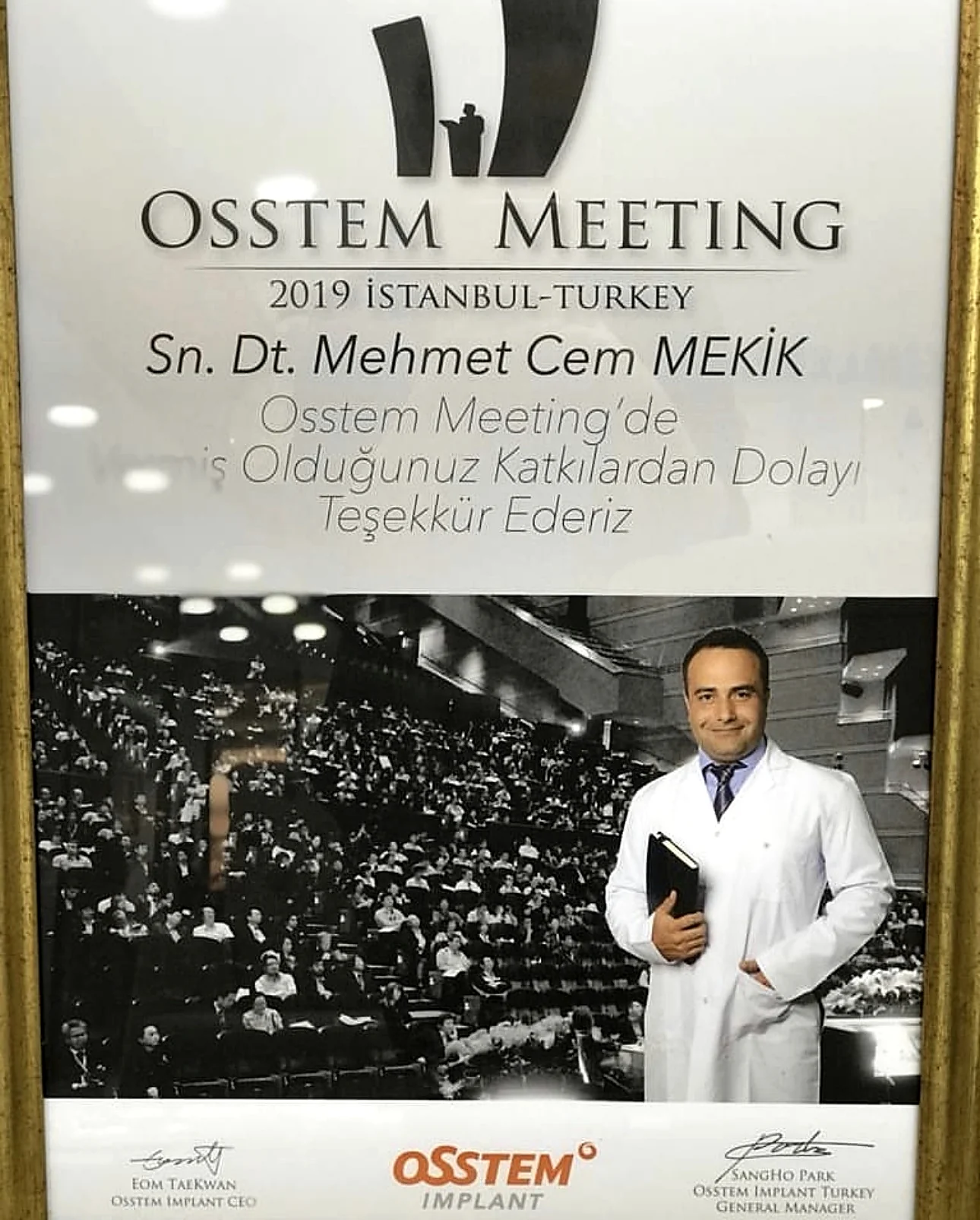 Çerçeveli bir Osstem Meeting 2019 İstanbul plaketi; üzerinde kalabalık bir amfi salonunda konuşma yapan bir hekimin fotoğrafı var